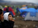Malý uprchlík si hraje s bublifukem v beneckém táboe u vsi Idomeni na...