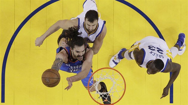 Steven Adams (v modrm) z Oklahoma City zakonuje na ko Golden State, brn ho Andrew Bogut (nahoe) a Draymond Green.