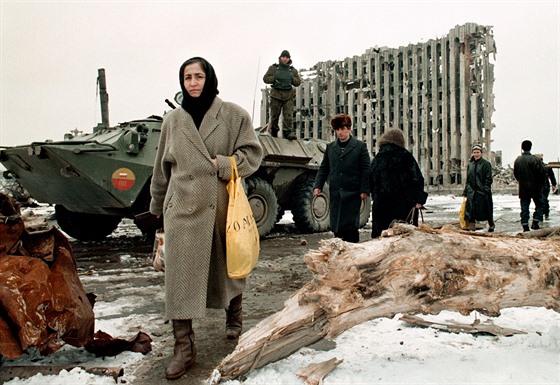 Čečenská žena míjí ruský obrněný transportér, v pozadí zničený prezidentský...