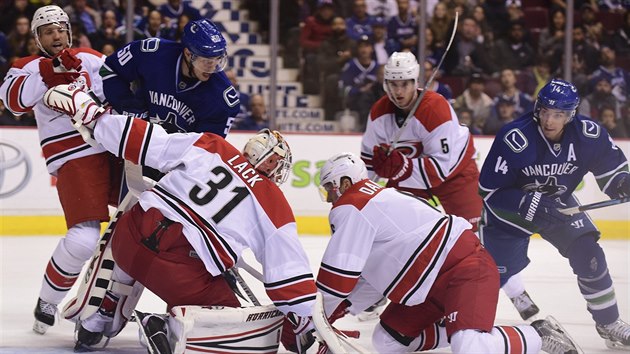 Eddie Lack v brance Caroliny se mus ohnt. Dotraj na nj Brendan Gaunce (druh zleva) a Alexandre Burrows (vpravo) z Vancouveru. Brnit pomh Klas Dahlbeck (klec).