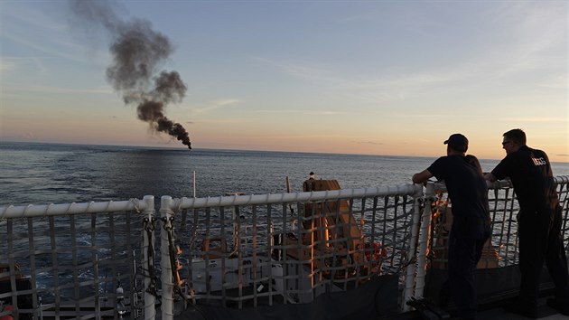 Hustý černý dým stoupá ze zapálené pašerácké lodi. Pobřežní stráž ji později potopila (23. února 2017)