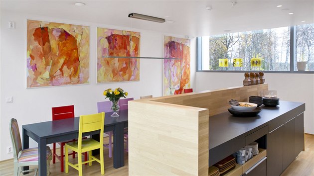 Místnost rozjasňují židle v oblíbených barvách majitelky a zářivé obrazy místní umělkyně. Kuchyň je v antracitové barvě.