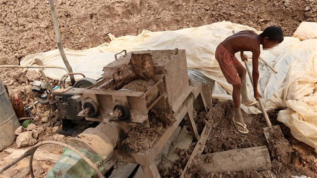 Kambodžský chlapec hází hlínu do stroje na výrobu cihel