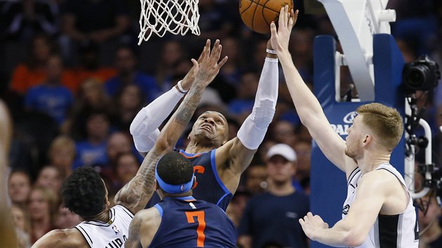 Russell Westbrook (uprosted) z Oklahoma City zakonuje v tlaenici na ko San Antonia. Brn mu Dejounte Murray (vlevo) a Davis Bertans.