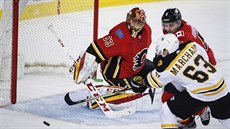 Gólman Calgary David Rittich pozorn sleduje, co s pukem provede Brad Marchand...