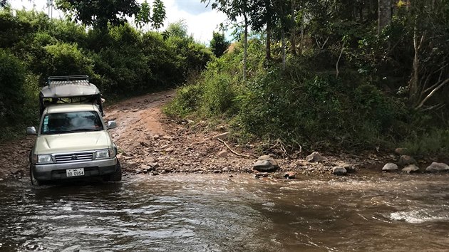 Cestu k pralesu ztěžuje protékající říčka. Řidiči pick-upů ji ale zkušeně překonají.