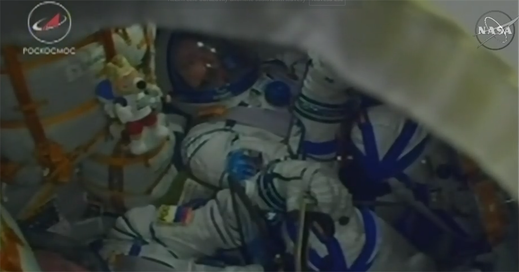 Posádka kosmické lodi Sojuz MS-08 během startu 21.3.2018. Krtečka připevněného k okraji křesla zakrývá výrazně větší maskot výpravy.