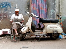 Amin, who paints repaired Vespa scooter parts, reads a newspaper outside his...