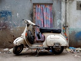 A Vespa scooter stands near a workshop, where old Vespa parts are painted, on...