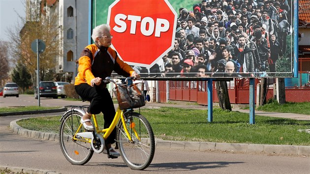 Žena v Gyongyosu projíždí na kole kolem protiimigračního předvolebního billboardu maďarského premiéra Viktora Orbána. (8. dubna 2018)