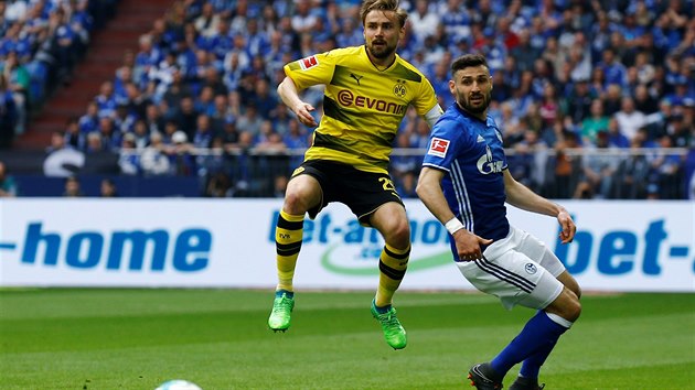 Marcel Schmelzer z Dortmundu (vlevo) a Daniel Caligiuri ze Schalke se ohlížejí za míčem a chystají se pro něj vystartovat.