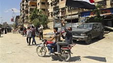 Syrští muži projíždějí na motocyklu s národní vlajkou poté, co syrské policejní...