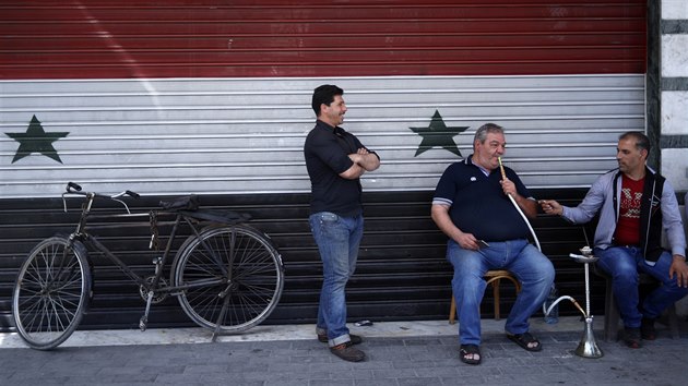Obyvatelé Damašku před obchodem s roletou v barvách syrské vlajky (17. dubna 2018)