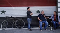 Obyvatelé Damaku ped obchodem s roletou v barvách syrské vlajky (17. dubna...