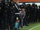 Jablonecký trenér Petr Rada sleduje zápas s kordonem policist za zády.
