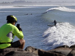 METROVÉ VLNY. Pozorovatel fotografuje surfaře na pláži Sumner Beach u města...