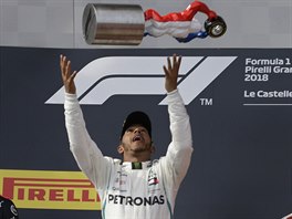 Lewis Hamilton (uprostřed) si na pódiu pohazuje s trofejí pro vítěze Velké ceny...