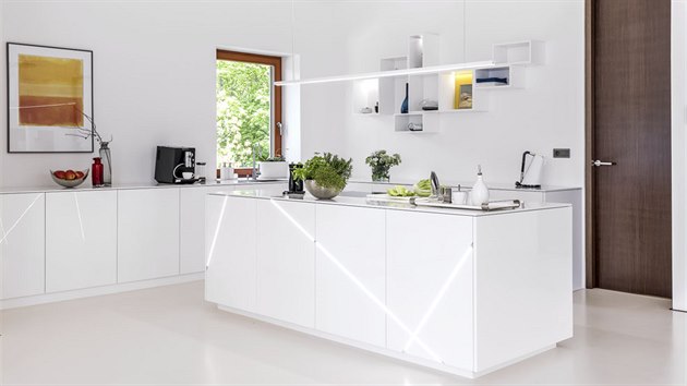 Bílou kuchyň oživují akcenty černé, dijonské žluté a zajímavě instalované osvětlení. Je vybavena spotřebiči Siemens.
