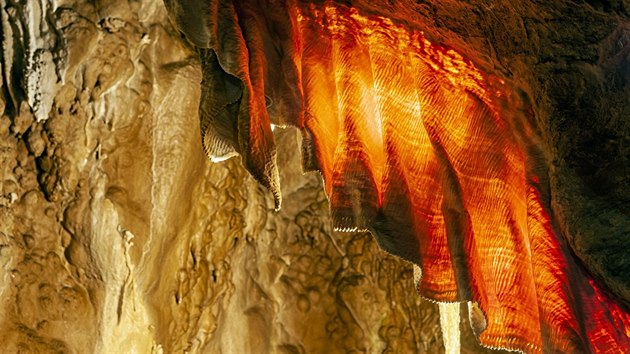 Pohled na jeden ze symbolů Javoříčských jeskyní - úchvatnou Záclonu. Dva metry dlouhý, 60 centimetrů široký a místy až čtyři milimetry silný útvar pojmenovaný podle svého vzhledu je na okraji ozdoben i jakousi krajkou, jejíž vzorky tvoří plochy krystalizujícího kalcitu, a při nasvícení celá dostává sytě rudé zbarvení, což je způsobeno příměsí oxidů železa.