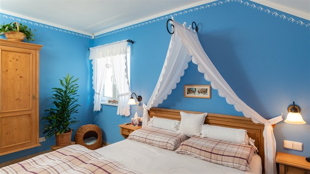 Každá místnost vítá jedinečnou atmosférou a barevnou škálou. Ložnice uklidňuje modro-bílou v kombinaci s kontrastním dřevěným masivním nábytkem.