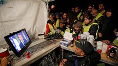 Demonstranti z uskupení lutých vest sledují proslov francouzského prezidenta...