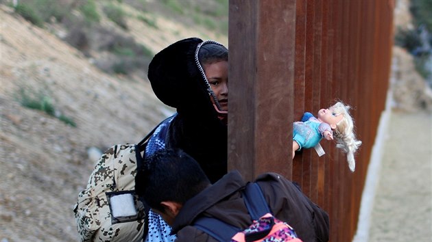 Migranti překonávají hraniční plot na americko-mexické hranici. (27. prosince 2018)