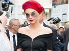 Modelka Cara Delevingne v rudém baretu s nápisem, pod kterým má schované vlasy....