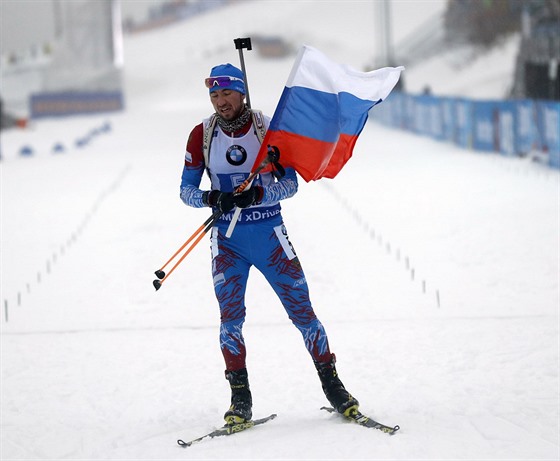 Rus Alexandr Loginov dojídí s vlajkou do cíle muské tafety v Oberhofu.