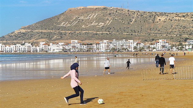 Na pli v Agadiru se d spatit leccos, dokonce i mlad muslimky, jak hraj fotbal. V pozad je vidt vrch, kde stvala pevnost (kasba). V roce 1960 ji stejn jako cel msto zniilo zemtesen.