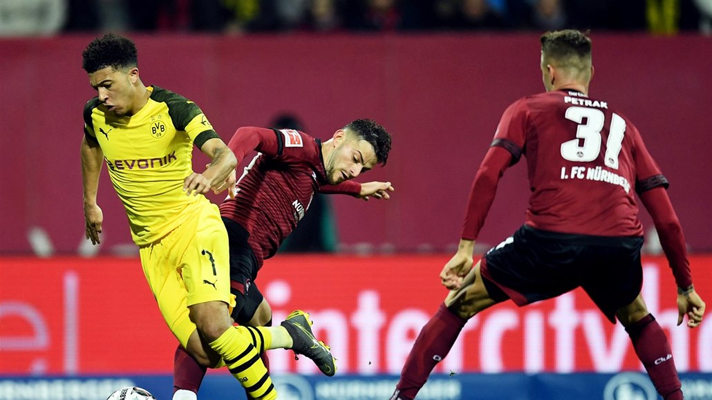 Jadon Sancho (vlevo) z Dortmundu kličkuje kolem Lukase Muhla (uprostřed) a...