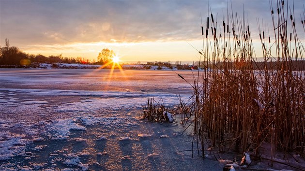 Slunce zapadajc nad stle jet zamrzlm jezerem Chomoutov na Olomoucku. (4. nora 2019)