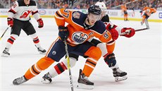 Connor McDavid z Edmontonu si kryje puk, brání ho Andy Greene z New Jersey.