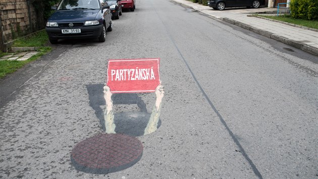 Ruce čouhající z odklopeného kanálu a svírající tabulku s názvem ulice Partyzánská.