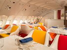 Interiér luxusního letadla zdobí barevná kesílka a stolky s bílými ubrusy.