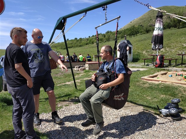 Paraglidová sedačka v houpačce. V pravé ruce záložní padák.
