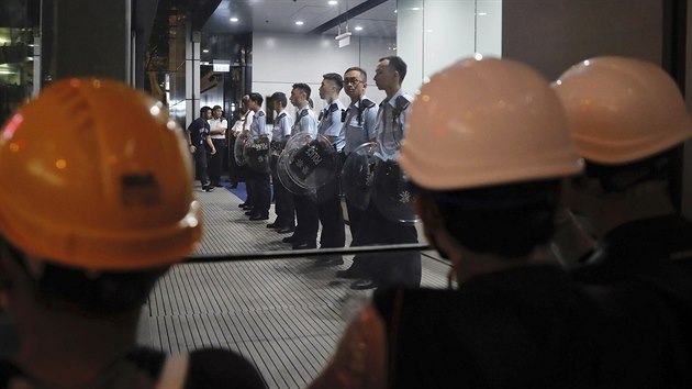 Policist stoj uvnit policejnho sdla, zatmco se demonstranti shromauj venku.