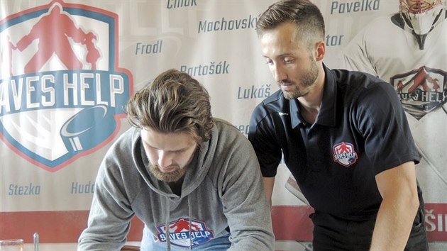 Podpis pro dobrou věc Hokejový brankář Šimon Hrubec sleduje Patrika Bartošáka, jenž podepisuje dres s logem Saves Help, který půjde do dražby, jejíž výtěžek se odešle na dobročinné účely.
