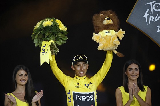 Vítz Tour de France Egan Bernal z Ineosu slaví na pódiu s kyticí a plyákem.
