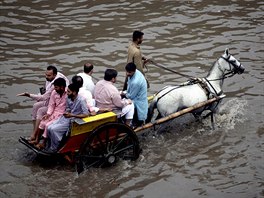 POVODN. Pákistánci se po deti vezou na koském povozu zaplavenou ulicí msta...