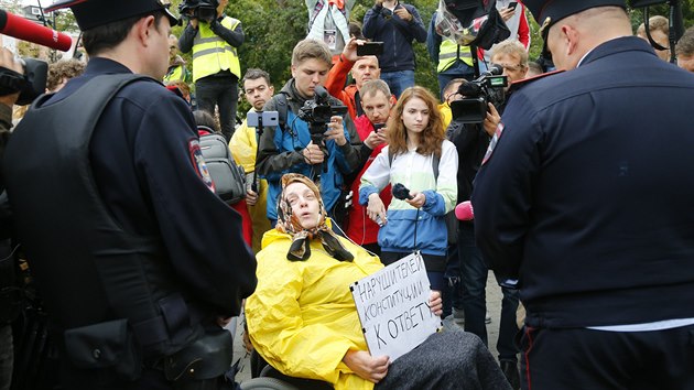 Aktivistka na invalidním vozíku mluví během protestu s policisty. V ruce drží ceduli s nápisem: „Ti, co porušují ústavu, nechť jsou předáni spravedlnosti.“ (17. srpna 2019)