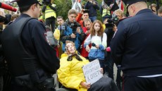 Aktivistka na invalidním vozíku mluví bhem protestu s policisty. V ruce drí...