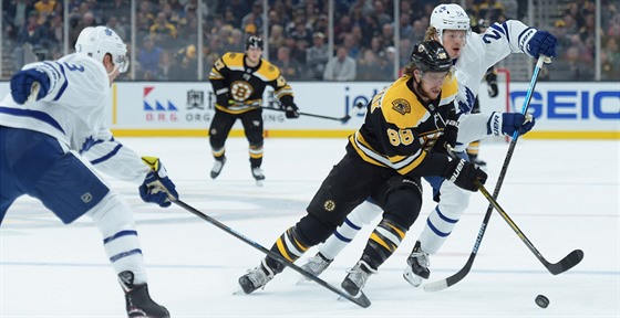 David Pastrák z Boston Bruins klikuje s pukem mezi Justinem Hollem (vlevo) a...