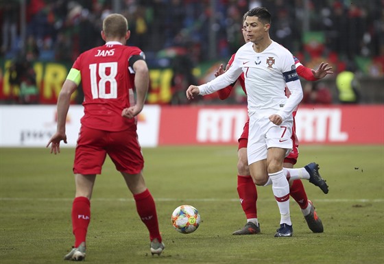 Portugalec Cristiano Ronaldo (v bílém) vede balon mezi lucemburskými hrái...