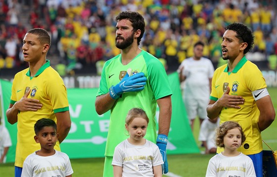 Braziltí fotbalisté Richarlison, Alisson a Marquinhos (zleva) zpívají pi...