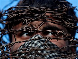 A masked Kashmiri man with his head covered with barbed wire attends a protest...