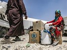 Dívka sedí vedle balík humanitární pomoci v táboe Al-Húl. (22. ervence 2019)