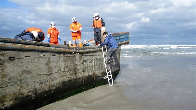 Japonští vyšetřovatelé ohledávají těla osmi severokorejských rybářů na lodi, kterou moře vyplavilo na pláž u města Oga. (27. listopadu 2017) 