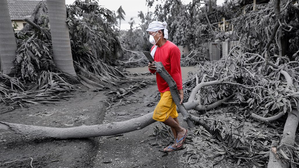 Muž odklízí polámané větve ve filipínském letovisku Talisay, které pokryl popel...