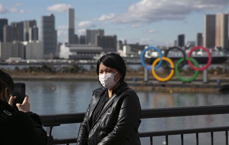 Turistka pózuje v Tokiu ped olympijskými kruhy s ochrannou roukou na tvái.