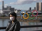 Turistka pózuje v Tokiu před olympijskými kruhy s ochrannou rouškou na tváři.